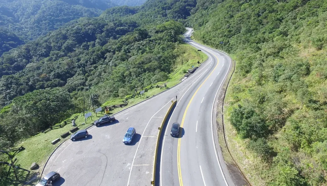 Rodovia de pista dupla cortando área de mata em região serrana