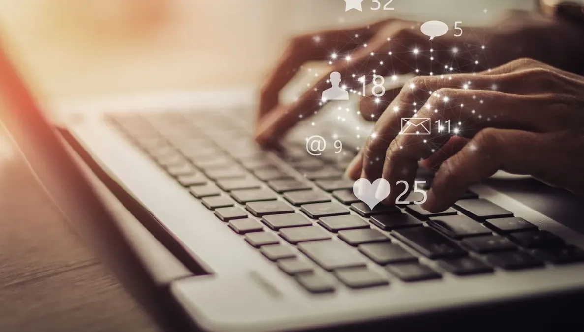 Mãos digitando em notebook com ícones de interações flutuando